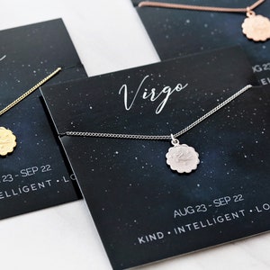 May include: Three necklaces with zodiac signs on a black background with stars. The necklaces are gold, silver, and rose gold. The signs are Virgo, with the dates August 23 - September 22 and personality traits listed below.