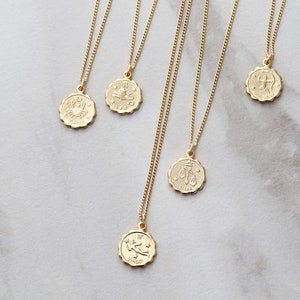 May include: Five gold necklaces with zodiac signs as pendants. The pendants are round and have a raised design. The signs are: Cancer, Leo, Libra, Sagittarius, and Virgo.