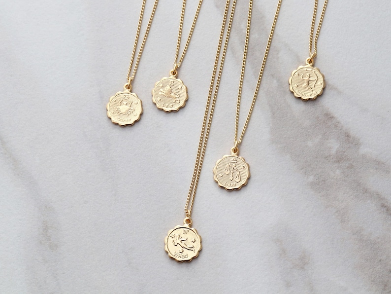 May include: Five gold necklaces with zodiac signs as pendants. The pendants are round and have a raised design. The signs are: Cancer, Leo, Libra, Sagittarius, and Virgo.