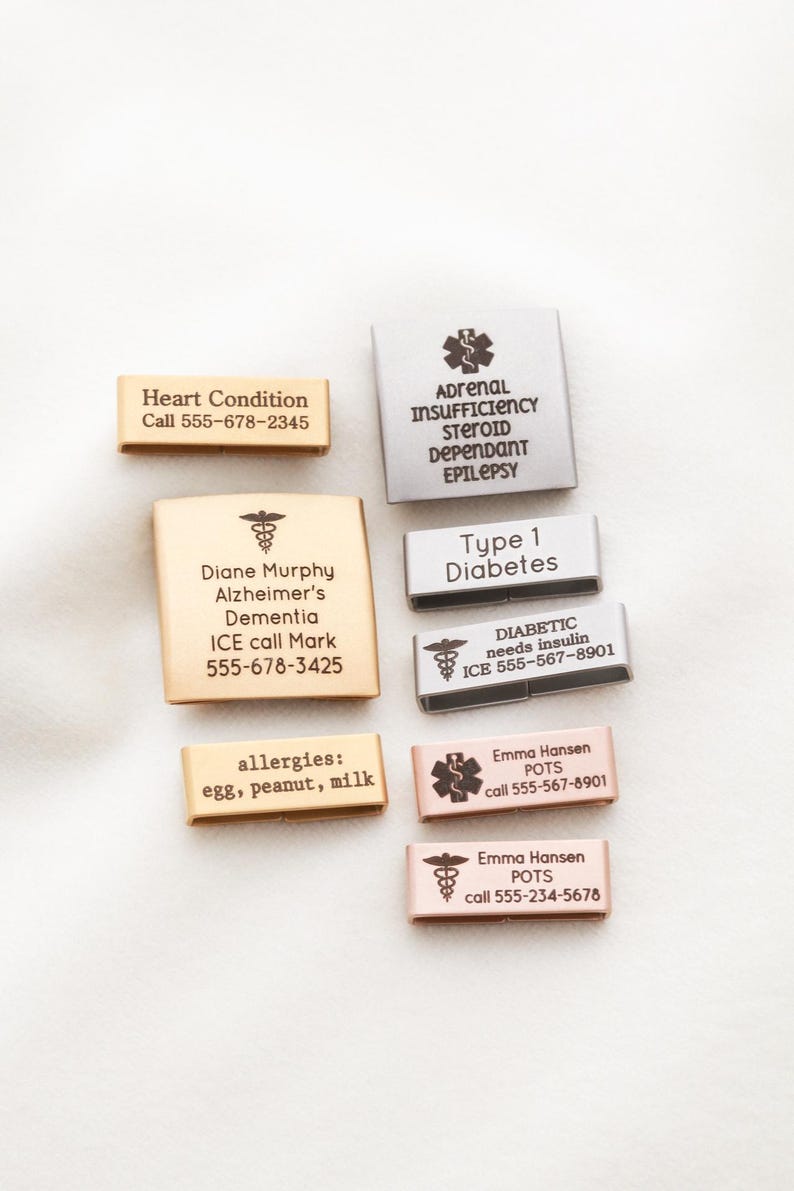 May include: A collection of rectangular medical alert watch band charms in gold, silver, and rose gold tones. Each charm features engraved medical information, including names, conditions like diabetes or epilepsy, and emergency contact phone numbers.