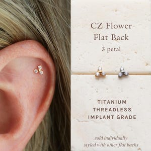 May include: A close-up of an ear with a gold CZ flower flat back earring. The earring has three clear crystal petals. The text on the right says "CZ Flower Flat Back 3 petal TITANIUM THREADLESS IMPLANT GRADE".