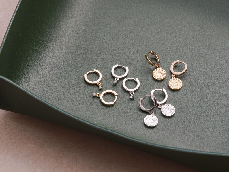 May include: A set of six gold and silver hoop earrings with a small dangling charm. Each charm is a circular design with a raised center and a small clear stone.