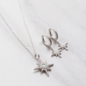 May include: A silver necklace and earrings set featuring a starburst pendant and matching earrings with opal accents. The jewelry is on a white background.