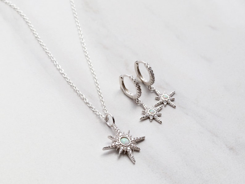 May include: A silver necklace and earrings set featuring a starburst pendant and matching earrings with opal accents. The jewelry is on a white background.