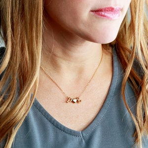 May include: A gold necklace with a heart charm and the letters "P" and "S" hanging from it. The necklace is worn by a person with long blonde hair.
