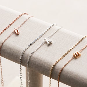 May include: Three delicate necklaces with initial charms. The necklaces are made of silver and rose gold chains with small round beads. The charms are in the shape of the letters 'E', 'K', and 'M'.