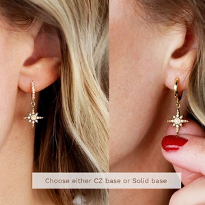 May include: Two gold earrings with a star-shaped charm. The earrings are shown on a model's ear. Choose either CZ base or Solid base.