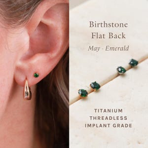 May include: Gold hoop earrings and emerald green stud earrings are shown on an ear. The image also displays several emerald green stud earrings with gold settings. Text on the image reads "Birthstone Flat Back May - Emerald" and "Titanium Threadless Implant Grade."