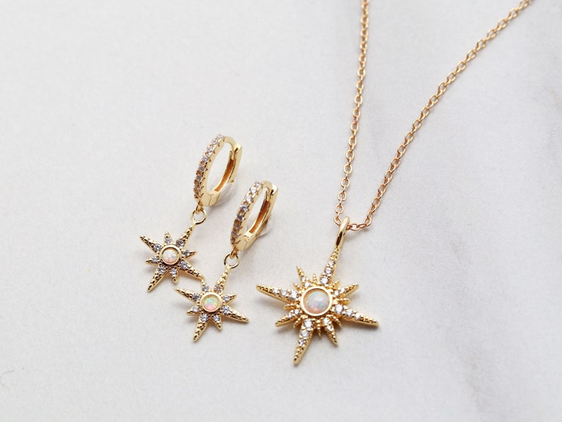 May include: A gold necklace and earrings set featuring a starburst design with a white opal center and clear crystal accents.