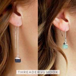 May include: Two pairs of earrings with different styles: a silver threaded earring with a black stone and a silver hook earring with a light blue stone. The text "THREADER vs HOOK" is below the earrings.