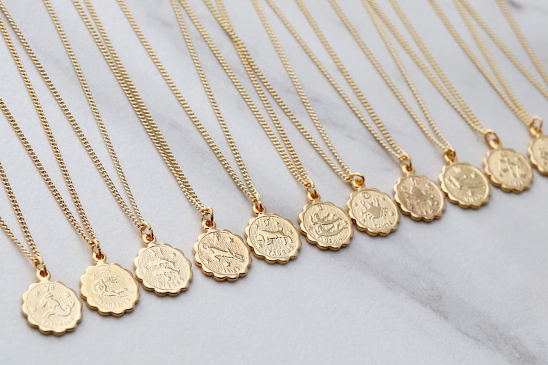 May include: A set of 12 gold zodiac necklaces with a chain and a pendant featuring a zodiac symbol. The pendants are round and have a scalloped edge.