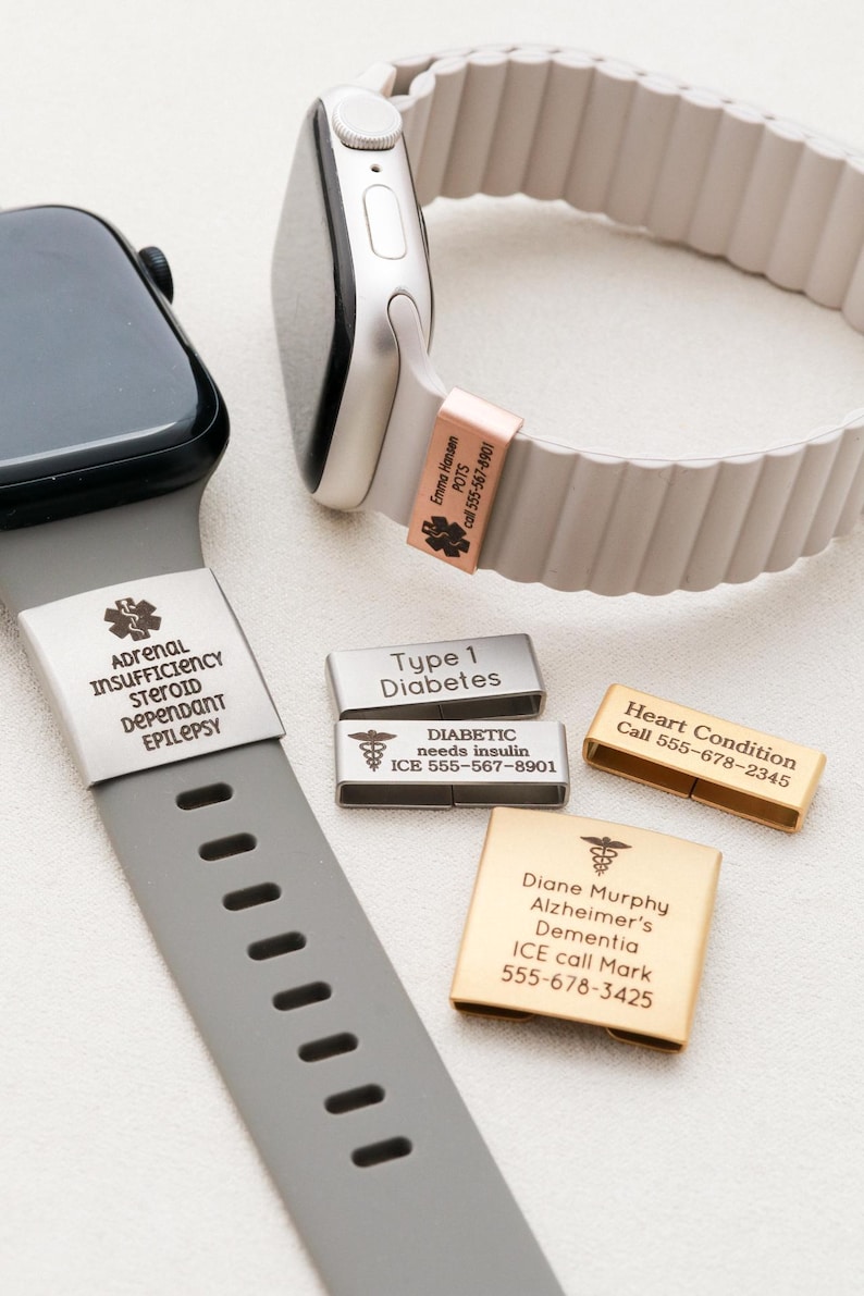 May include: Two smartwatches with medical alert bands attached, one grey and one beige. The grey band features a silver tag with medical text. The beige band has a rose gold tag. Three additional metal medical alert tags are shown in silver and gold.