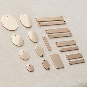 May include: A collection of gold-toned metal jewelry components including various sizes of circular discs and rectangular bars, each featuring small pre-drilled holes for attachment, arranged in a grid-like pattern on a light surface.