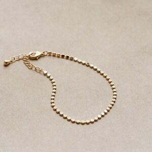 May include: A gold chain bracelet with a delicate, round link design. The bracelet is made of a thin chain and has a simple, elegant style.