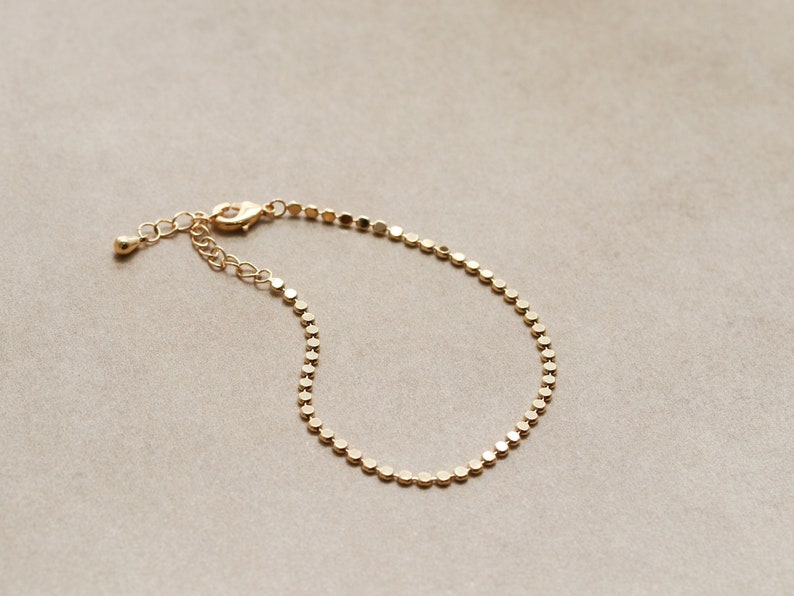 May include: A gold chain bracelet with a delicate, round link design. The bracelet is made of a thin chain and has a simple, elegant style.