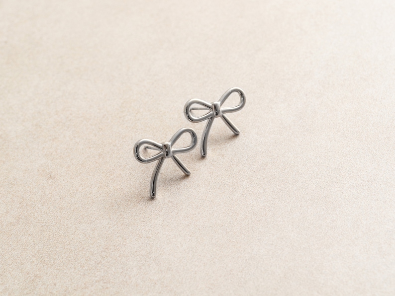 May include: A pair of silver bow-shaped earrings.