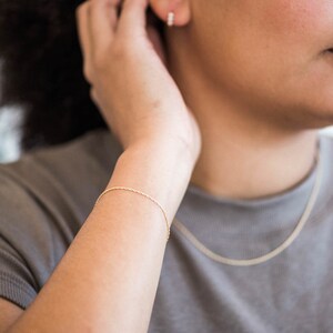May include: A gold chain bracelet with a delicate, twisted design. The bracelet is worn on a person's wrist.