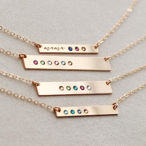May include: Four gold-toned bar necklaces with delicate chains. The top bar features the word mama in script and three small round gemstones. The other three bars feature varying sequences of small, colorful, round, embedded gemstones.
