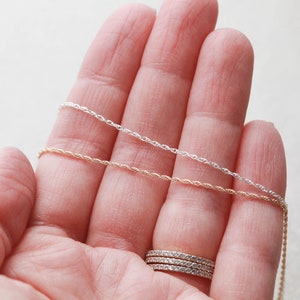 May include: Two silver and gold rope chains on a hand. The chains are different lengths and are held in place by the hand.