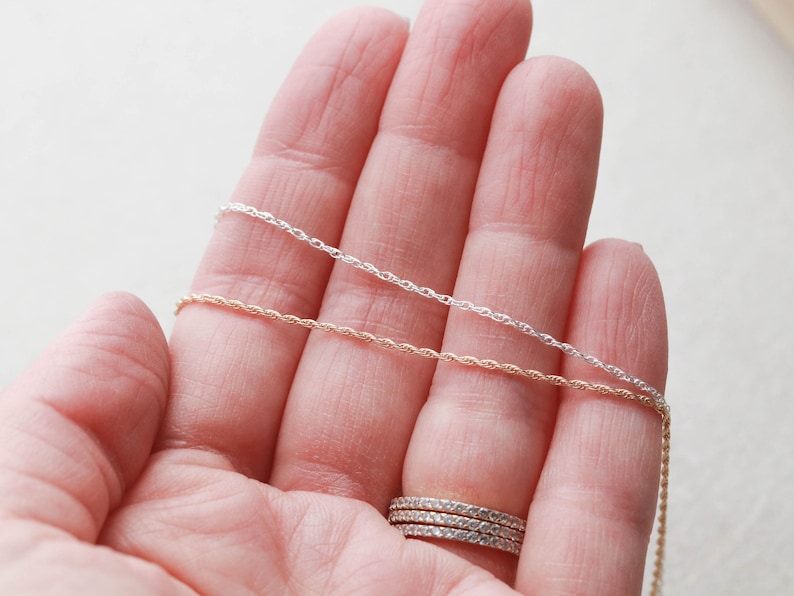 May include: Two silver and gold rope chains on a hand. The chains are different lengths and are held in place by the hand.