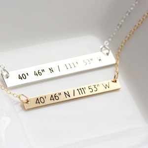 May include: Two necklaces with bar pendants. The pendants are engraved with the coordinates "40' 46" N / 111' 53" W". One necklace is silver and the other is gold.