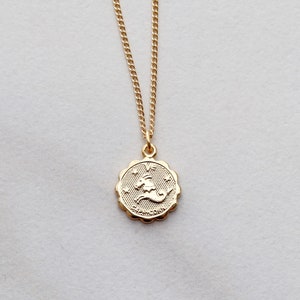 May include: Gold chain necklace with a gold pendant featuring the zodiac symbol for Capricorn.