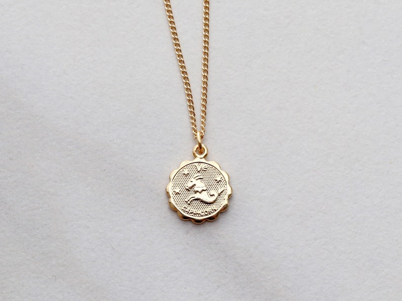May include: Gold chain necklace with a gold pendant featuring the zodiac symbol for Capricorn.