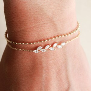 May include: A delicate gold bracelet with a chain and a row of small, clear stones set in a leaf design.