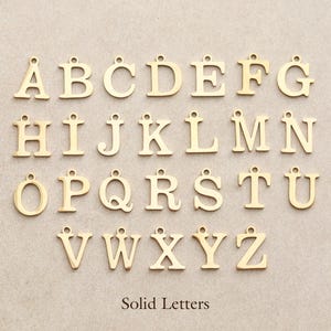 May include: Gold-colored solid letter charms, A through Z, with a small loop at the top for stringing. The letters are displayed on a neutral background. The text "Solid Letters" is at the bottom.