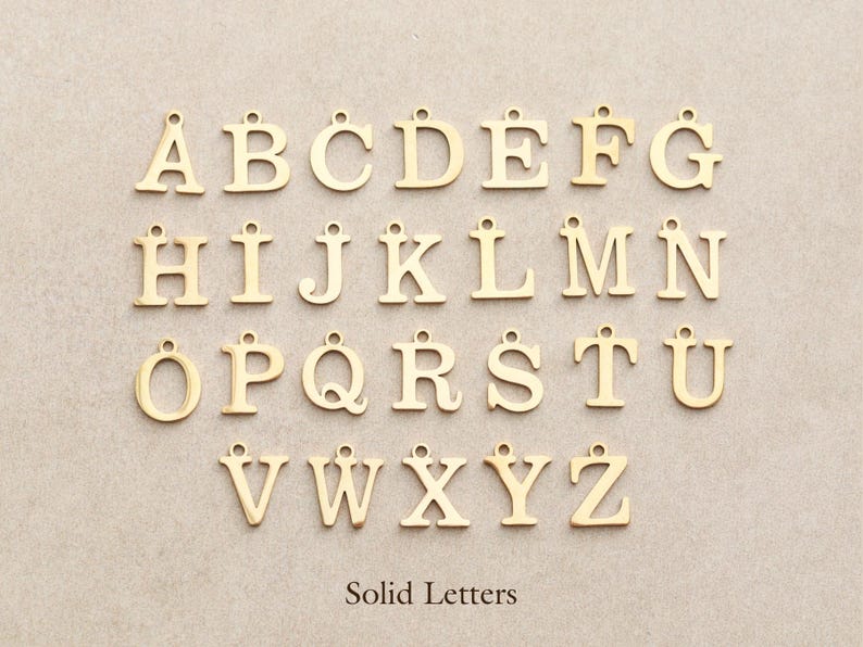 May include: Gold-colored solid letter charms, A through Z, with a small loop at the top for stringing. The letters are displayed on a neutral background. The text "Solid Letters" is at the bottom.
