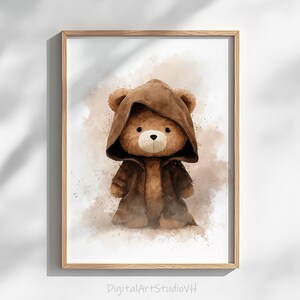 May include: Watercolor illustration of a teddy bear wearing a brown hooded cloak. The bear has a light brown fur with a white muzzle and a black nose. The artwork is framed in a wooden frame and has a watercolor background.