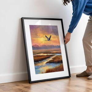 Crane in flight picture for coastal decor — realistic landscape artwork featuring golden grasses and winding marshland at sunset.