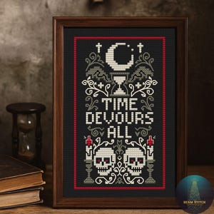 Peut inclure: Broderie au point de croix encadrée dans un cadre en bois foncé. Le fond noir présente le texte "TIME DEVOURS ALL" en blanc. Le motif comprend un croissant de lune, un calice, des crânes, des bougies et des ornements décoratifs. Une bordure rouge encadre le motif.