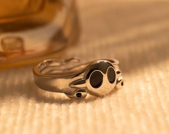 Könnte beinhalten: Ein silberner Ring mit einem Totenkopfdesign. Der Totenkopf hat zwei schwarze Augen.