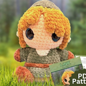 May include: A plush crochet doll featuring a large head with textured golden-yellow yarn hair, oversized dark eyes, and a peach-colored face. The doll wears a dark olive green tunic with a brown belt and matching brown boots, accompanied by a PDF pattern.
