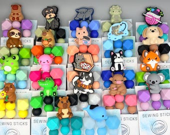 May include: A collection of colorful silicone beads and charms in various animal shapes, including bears, dogs, cats, and a whale. The beads are arranged in rows with geometric shapes and are suitable for crafting.
