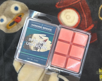 May include: A clear plastic package containing six coral-colored wax melts. The package also includes a label with the text "Hanging Bridge" and "Into the Unknown" with a graphic of a bird. Net weight is 2.5 oz.