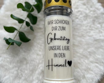 Può includere: Una candela di vetro bianco con un coperchio dorato e una scritta nera che dice "Wir schicken dir zum Geburtstag unsere Liebe in den Himmel" con un cuore nero.