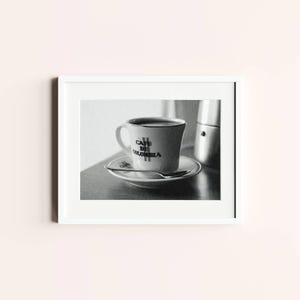 Può includere: Fotografia in bianco e nero incorniciata di una tazza e un piattino da caffè. La tazza riporta la scritta "Cafe de Colombia". Un cucchiaino è appoggiato sul piattino. Sullo sfondo si vede una caffettiera.