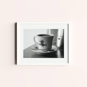 Peut inclure: Photographie encadrée en noir et blanc d'une tasse et d'une soucoupe à café. La tasse, remplie de liquide foncé, porte l'inscription "CAFE DE COLOMBIA". Une cuillère repose sur la soucoupe. Une cafetière en métal est visible en arrière-plan.