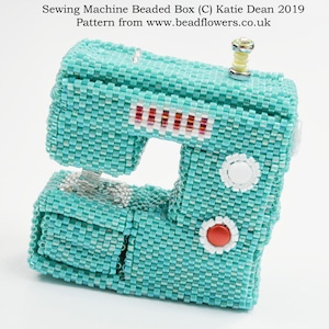 May include: A turquoise blue beaded sewing machine box with red, white, and silver accents. The box is made of small beads and has a detailed design.