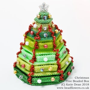 Op de afbeelding: Een groene, rode en witte kerstboomdoos van kralen. De doos is versierd met rode, witte en groene kralen. De bovenkant van de doos is een ster.