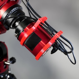 May include: A red telescope with a black lens and a red camera attached to it. The camera is connected to the telescope with black cables.