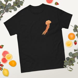 Peut inclure: T-shirt noir avec un motif de méduse orange aux tentacules rouges.