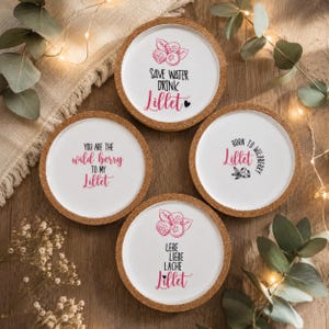 Könnte beinhalten: Vier runde Untersetzer aus Kork mit weißer Mitte, verziert mit Beerenillustrationen sowie Texten in Pink und Schwarz. Die Aufschriften lauten: Save Water Drink Lillet, You Are The Wild Berry To My Lillet, Born To Wildberry Lillet und Lebe Liebe Lache Lillet.