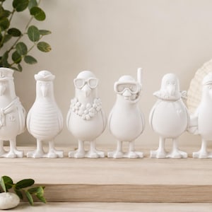 Könnte beinhalten: Ein Set aus sechs weißen, matten Möwenfiguren, die in einer Reihe stehen. Jeder Vogel ist mit verschiedenen Accessoires versehen, darunter eine Matrosenmütze mit Schal, ein gestreiftes Shirt, eine Blumenkette mit Sonnenbrille, eine Schnorchelausrüstung, ein Fisch und eine Wintermütze.
