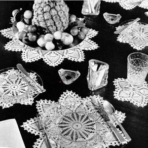 Puede incluir: Una foto en blanco y negro de una mesa puesta con manteles individuales de ganchillo, una piña y un vaso de agua. Los manteles individuales son blancos y tienen un delicado patrón de encaje. La piña está en un cuenco con fruta roja y verde. El vaso de agua está sobre un mantel individual.