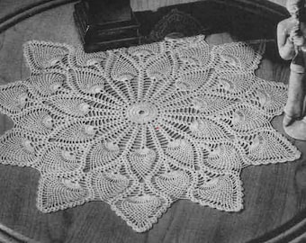 May include: A white crocheted doily with a starburst design. The doily is laid out on a wooden table.