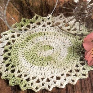 Puede incluir: Un encaje de ganchillo con un degradado de color verde y blanco. El encaje tiene una forma circular con un borde festoneado.