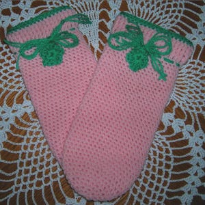 May include: A pair of pink crocheted oven mitts with green crocheted bows on the top.